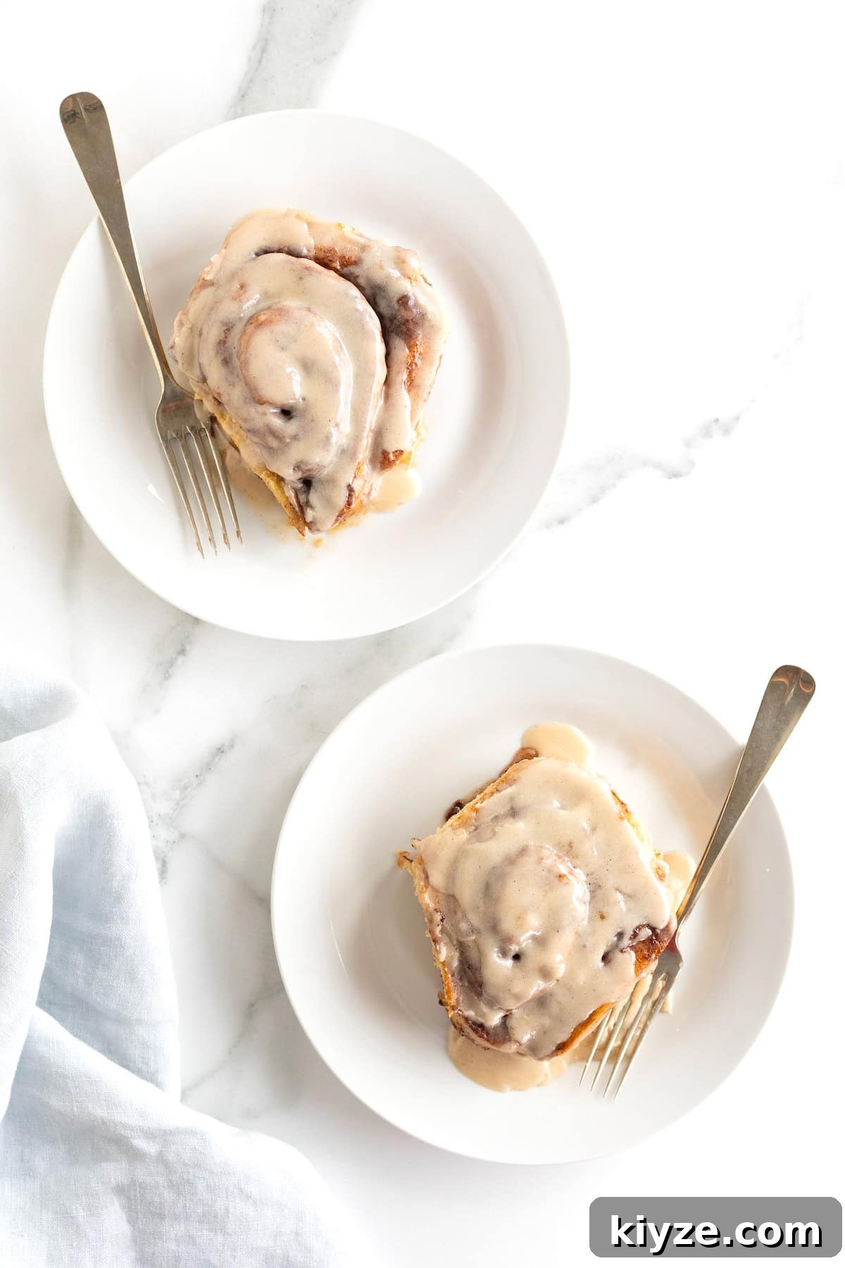 Quick Canned Cinnamon Rolls: Fast Oven & Air Fryer Hack 4 Two cinnamon rolls covered in icing on small white plates with forks.