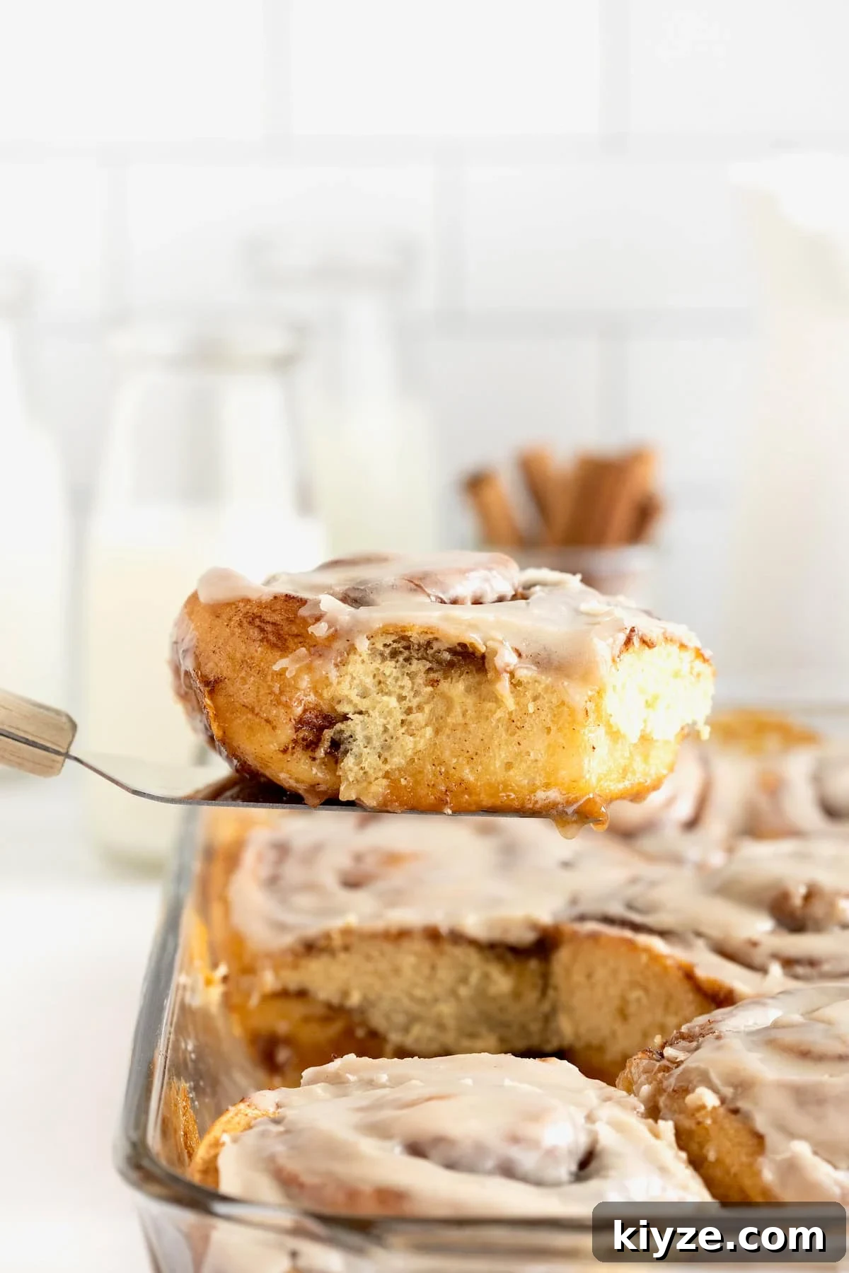 Quick Canned Cinnamon Rolls: Fast Oven & Air Fryer Hack 5 A cinnamon roll on a metal spatula above a glass baking dish of cinnamon rolls.