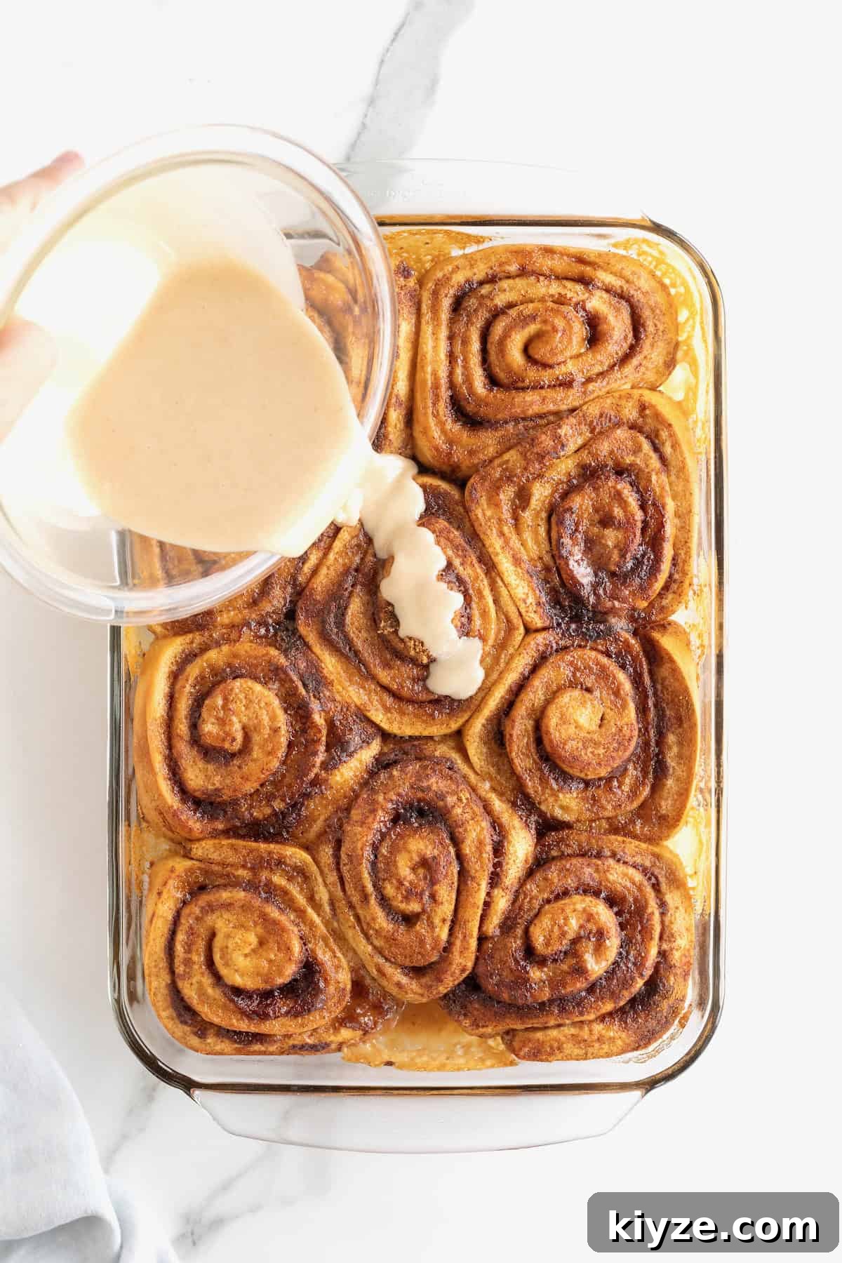Quick Canned Cinnamon Rolls: Fast Oven & Air Fryer Hack 9 Cinnamon vanilla icing being poured over baked cinnamon rolls in a glass baking dish.