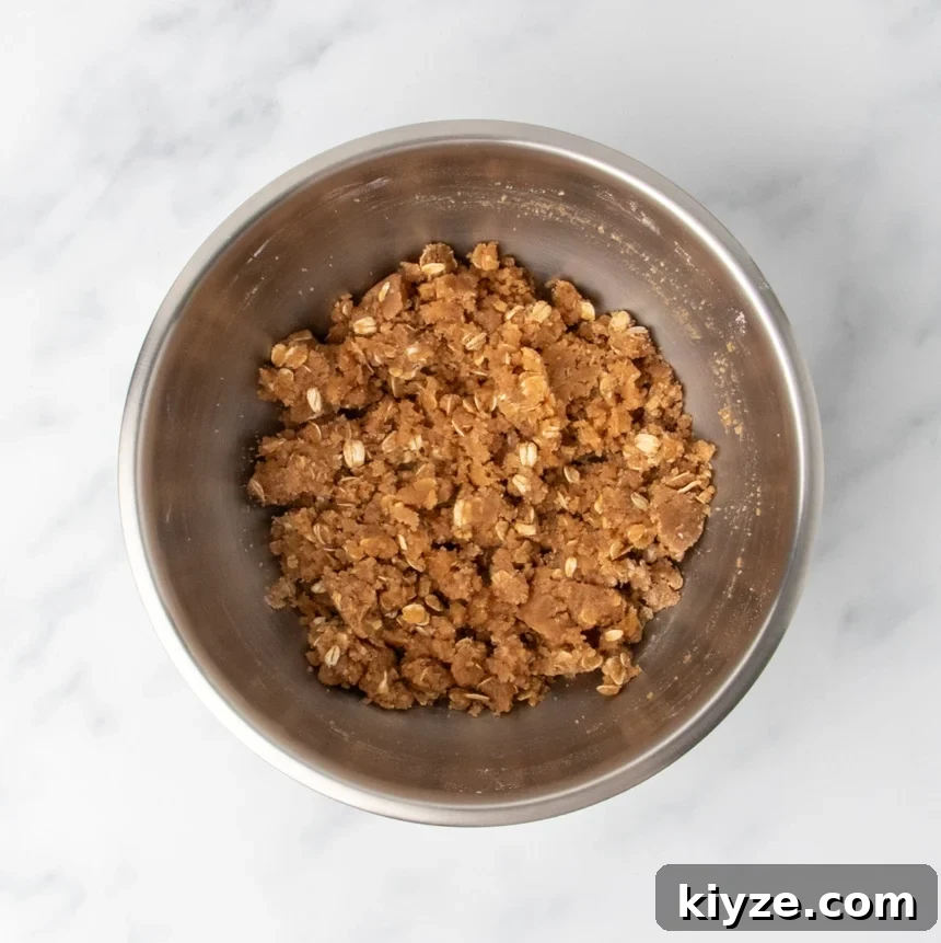 Gluten-Free Sweet Potato Casserole Recipe for Holidays 11 A metal mixing bowl filled with a dark brown, clumpy mixed oat and sugar topping mixture.