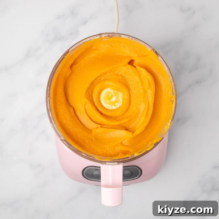 Gluten-Free Sweet Potato Casserole Recipe for Holidays 15 A top view of a food processor filled with smooth orange sweet potato mixture.