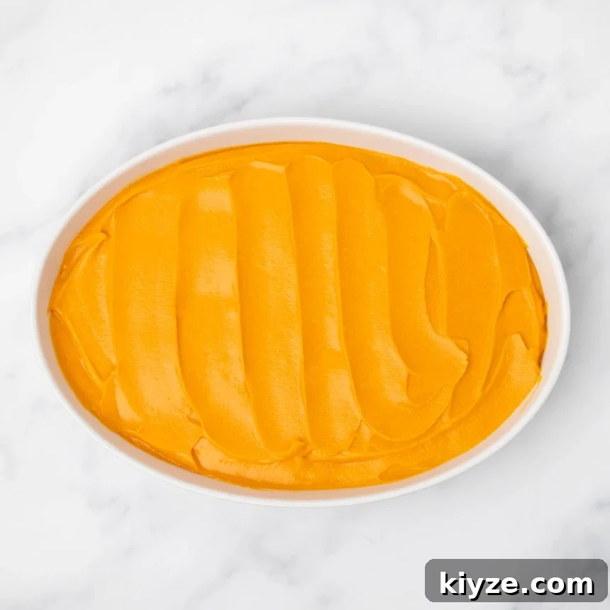 Gluten-Free Sweet Potato Casserole Recipe for Holidays 16 A white oval baking dish filled with evenly spread orange sweet potato filling on a white marble surface.
