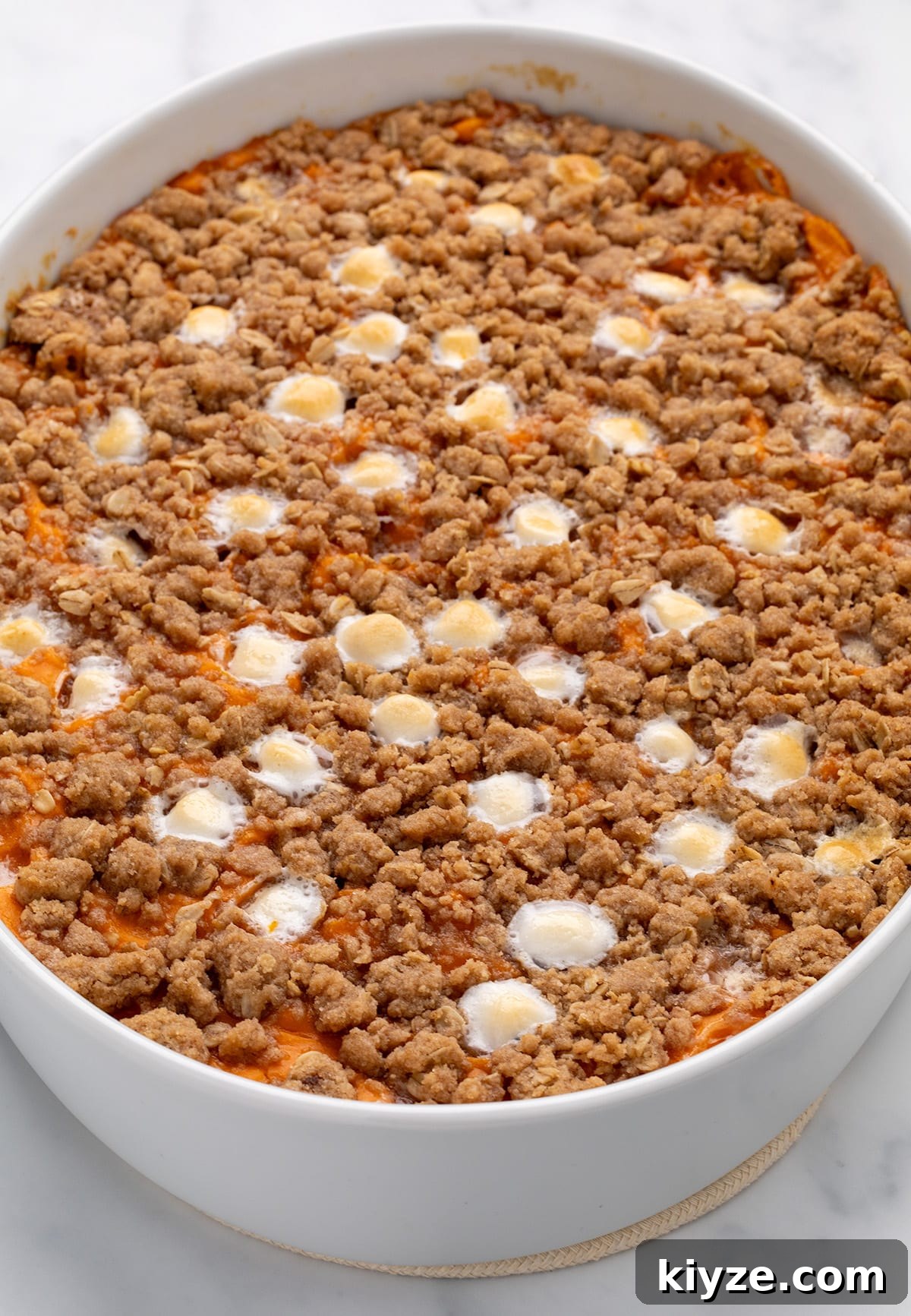Gluten-Free Sweet Potato Casserole Recipe for Holidays 21 A close-up of a baked gluten free sweet potato casserole in a white oval dish, showing a browned crumb topping with melted white marshmallows on the surface.