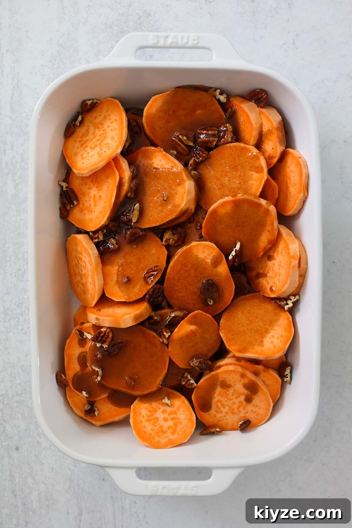 Bourbon-Glazed Candied Yams Recipe for Holiday Sides 4 sliced yams with sauce and pecans on top.