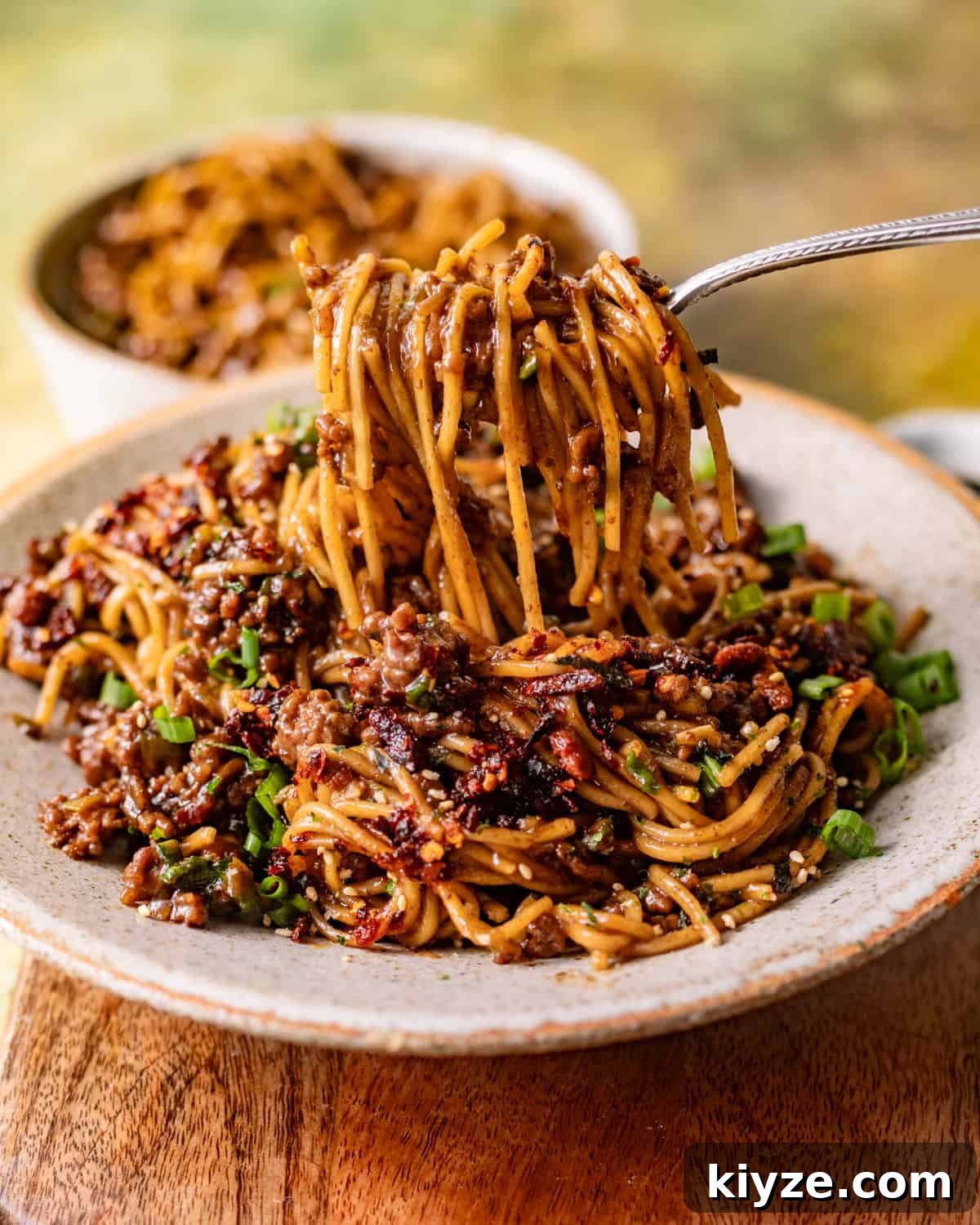 Mongolian Beef Noodles with Ground Beef and Scallions 2 saucy mongolian ground beef noodles in a bowl with a fork pulling the noodles out of the bowl.