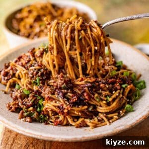 Mongolian Beef Noodles with Ground Beef and Scallions 13 saucy mongolian ground beef noodles in a bowl with a fork pulling the noodles out of the bowl.