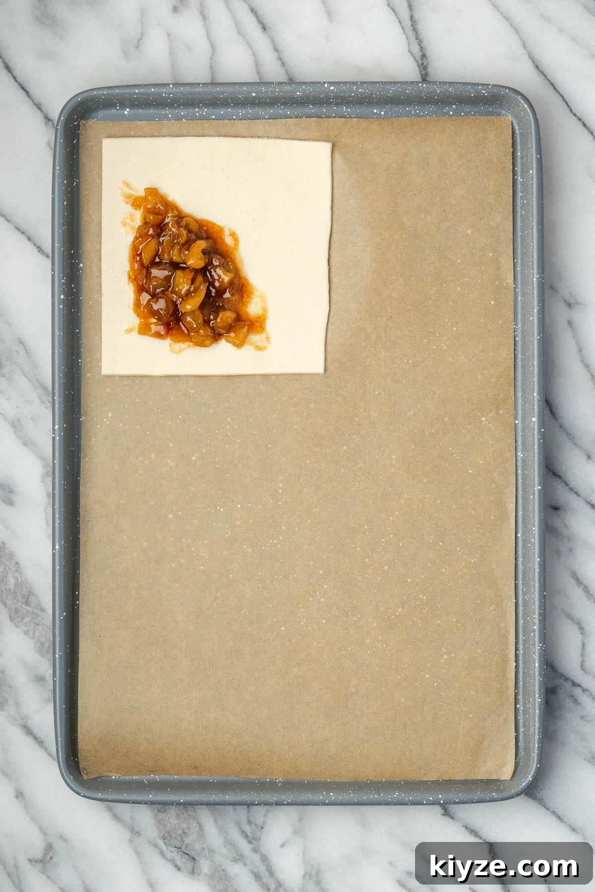 Flaky Apple Turnovers with Puff Pastry Recipe 7 A square of puff pastry with apple filling sitting on a baking sheet.