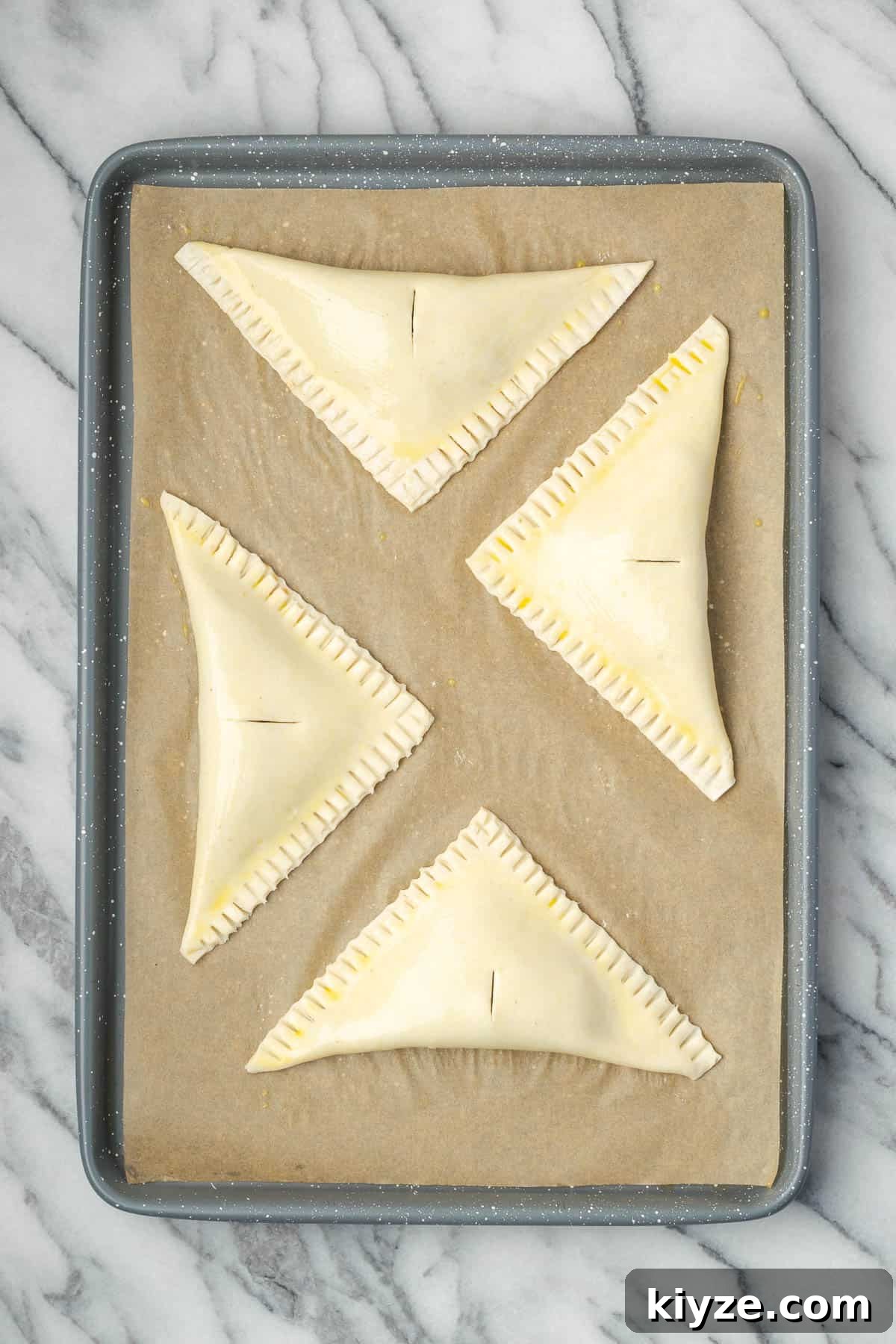Flaky Apple Turnovers with Puff Pastry Recipe 8 Four large apple turnovers sitting on a baking sheet.