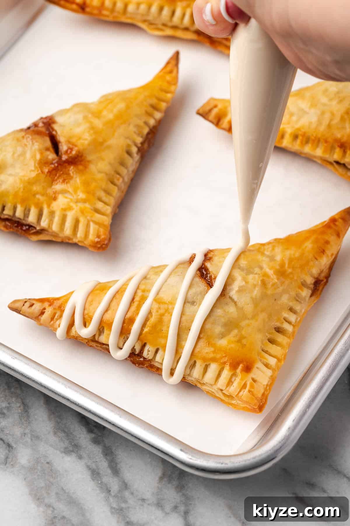Flaky Apple Turnovers with Puff Pastry Recipe 9 Icing being drizzled over freshly baked turnovers.