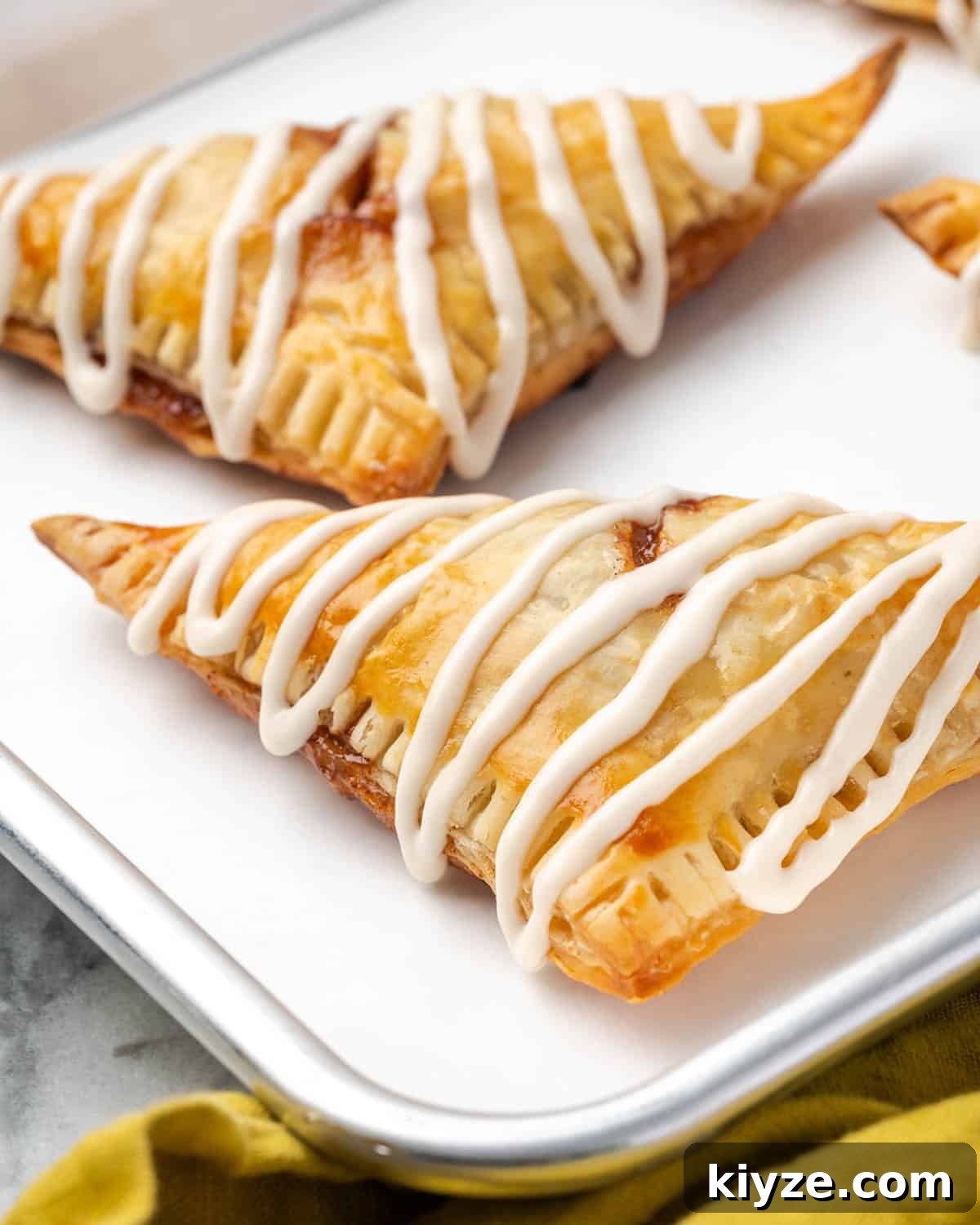 Flaky Apple Turnovers with Puff Pastry Recipe 10 Two apple turnovers made with puff pastry sitting on a metal tray.