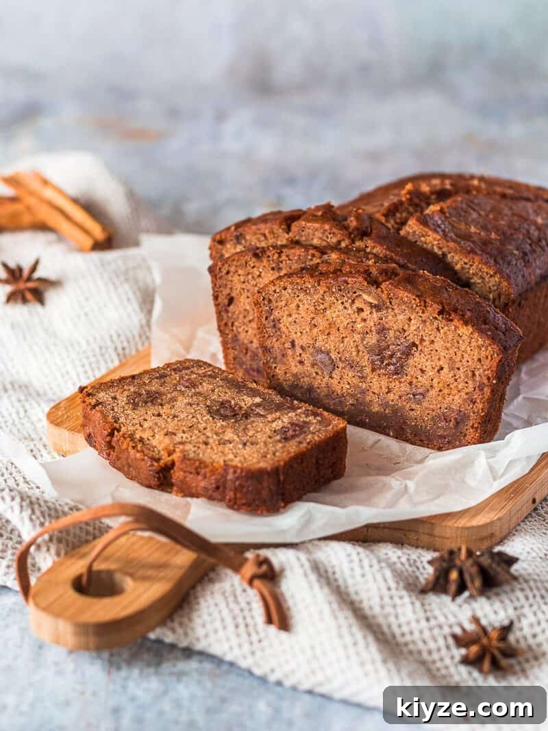 Classic Fruit Cake Loaf Recipe: Moist Holiday Fruitbread 2 A Fruit Cake Loaf on a sheet of white baking parchment paper on a wood cutting board. There are some whole spices in the background.