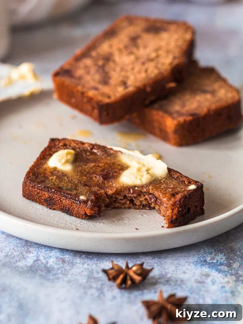 Classic Fruit Cake Loaf Recipe: Moist Holiday Fruitbread 4 Three slices of fruit cake loaf on a plate. Two slices are in the background, the slice in front is in focus, a bite has been taken and there is a layer of vegan butter spread onto it - it's melting!
