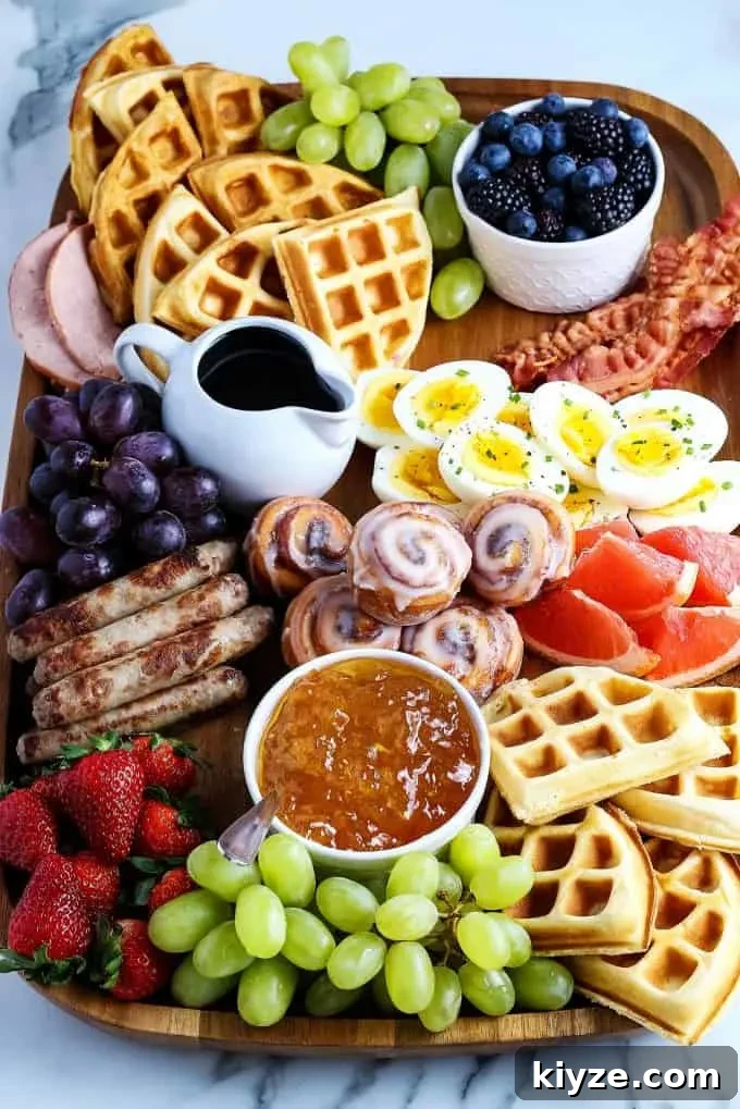 mini cinnamon rolls, deviled eggs, breakfast sausage, waffles, fruit, sausage links, Canadian bacon, and berries on a wooden board