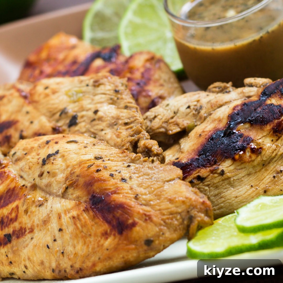 Zesty Basil and Lime Chicken Recipe for Tangy Weeknight Meals 2 Grilled chicken on a square plate, garnished with lime slices. A small clear glass cup of Dijon basil lime dipping sauce is on the plate.