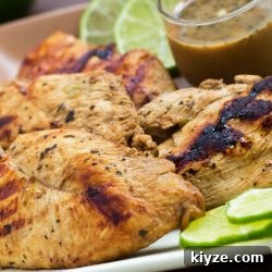 Grilled chicken on a square plate, garnished with lime slices. A small clear glass cup of Dijon basil lime dipping sauce is on the plate.