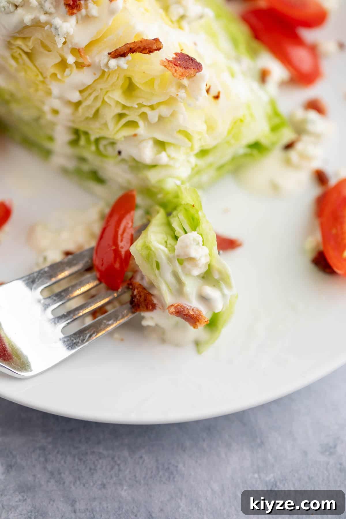 Classic Blue Cheese Wedge Salad with Crispy Bacon and Dressing 7 A bite of salad with tomatoes and bacon on a fork.