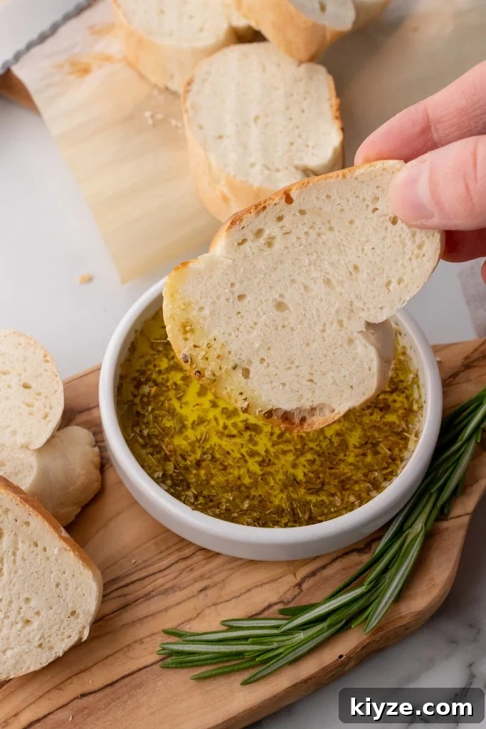30-Minute Crusty Baguettes: Foolproof Recipe for Homemade Bread 14 a hand dipping a slice of 30 minute french bread into a shallow white bowl filled with dipping oil