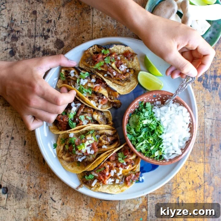 A hand putting onions and cilantro on mushroom tacos