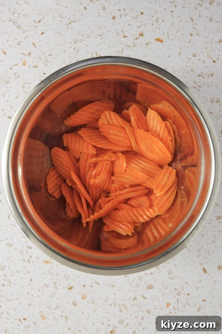 Crispy Air Fryer Carrot Chips Recipe 4 pre-sliced carrot chips in a metal bowl on kitchen counter