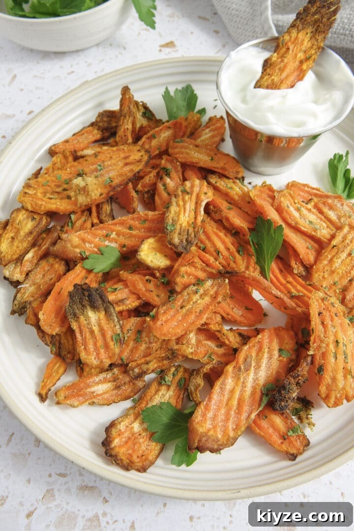 Crispy Air Fryer Carrot Chips Recipe 8 air fryer carrot chips on a plate with parsley and one carrot chip dipped in yogurt sauce