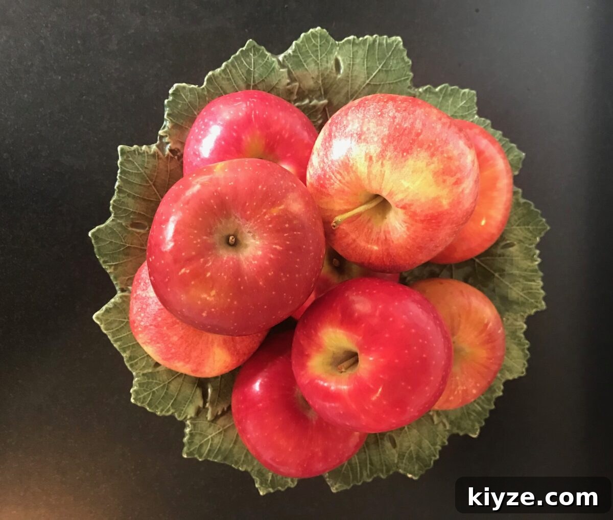 Green leafy ceramic pedestal dish with an assortment of fresh apples on top.