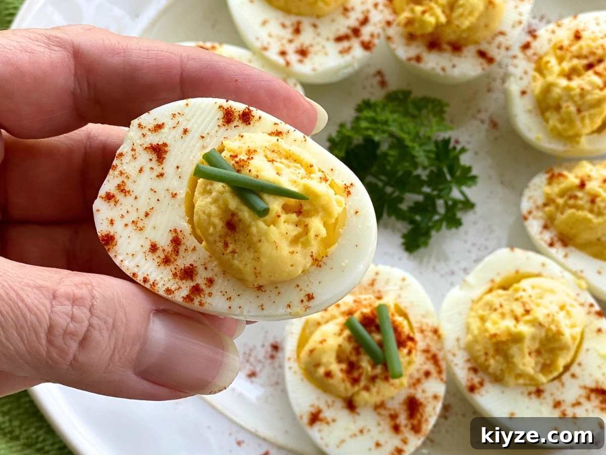 Hand holding a deviled egg over a plate with more eggs.