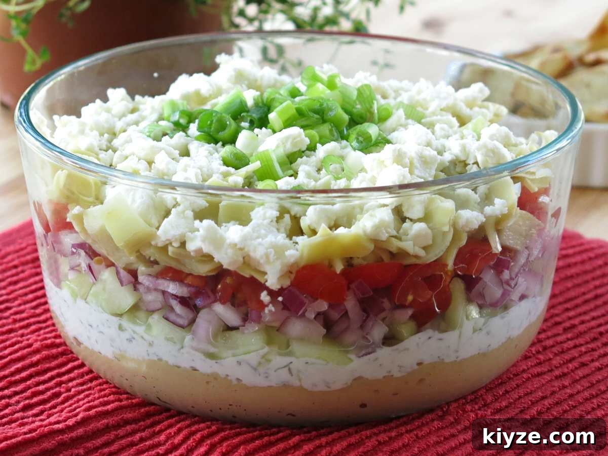 Seven layer Greek dip in a glass bowl exposing the seven layers.