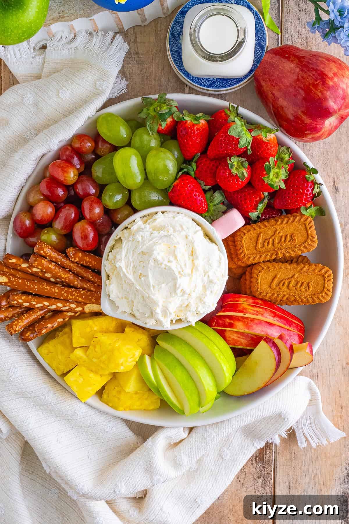 Easy Cream Cheese Fruit Dip Recipe with Cool Whip served in a pink bowl on a large wooden board with fresh strawberries, grapes, pineapple, apples, and graham crackers.