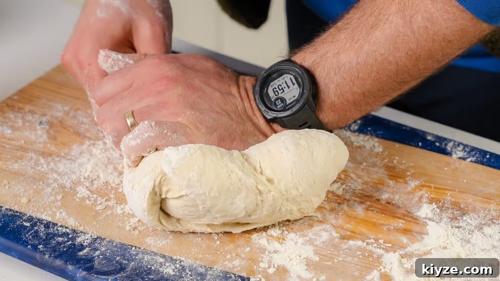 Homemade Pizza Dough Recipe for Crispy, Stretchy Crusts 2 The image captures the hands-on process of kneading homemade pizza dough. A person is seen working the soft, elastic dough on a flour-dusted wooden cutting board, pressing and folding it to develop the gluten. The dough appears fresh and pliable, ideal for stretching into a pizza base. The person's watch indicates the time, possibly suggesting a careful timing of the kneading process to ensure optimal texture. The scene conveys the tactile and meticulous nature of preparing pizza dough from scratch.