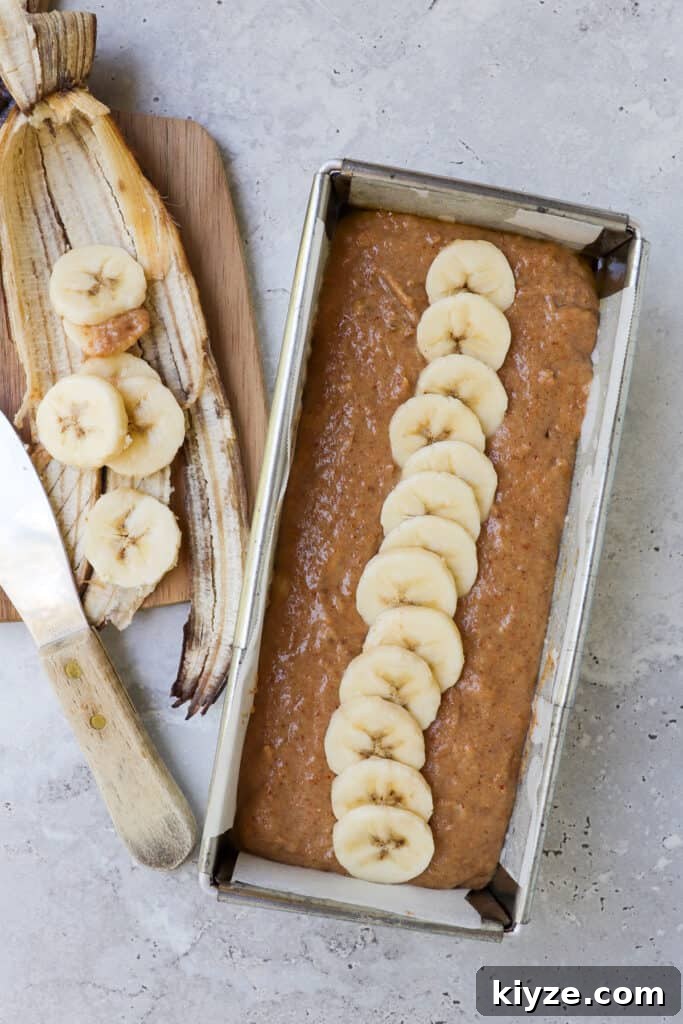 5-Ingredient Vegan Banana Bread Recipe 6 Bananas bread mixture in pan topped with banana sliced.