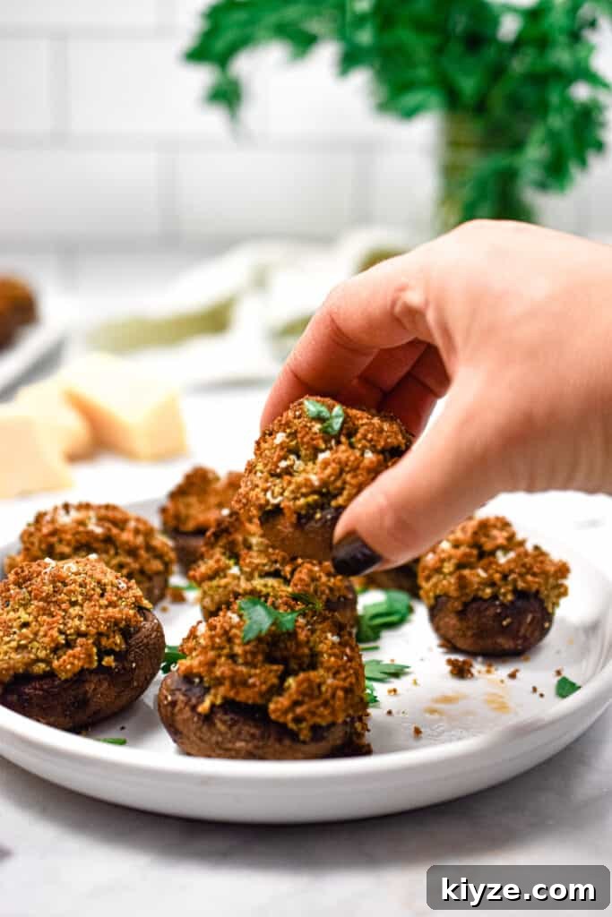 A hand is grabbing one of the Italian stuffed mushrooms off the plate