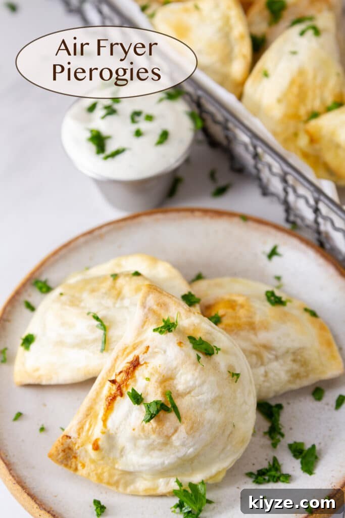 Crispy Air Fryer Pierogies with Garlic Butter Dipping Sauce 2 three pierogies on a white plate next to a dipping cup of ranch dressing and a basket of pierogies.
