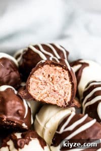 This Raspberry Cheesecake Truffles Recipe is super simple and great for baby showers, Valentine's Day, or as a gift for a friend or neighbor. The truffles are filled with fresh raspberries, whipped topping, cream cheese, graham crackers then covered in dark or white chocolate. This dessert is ready in about an hour, make ahead and freezer friendly! #desserts #recipe #ValentinesDay Strait on shot of raspberry truffle cut in half.