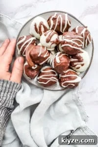 This Raspberry Cheesecake Truffles Recipe is super simple and great for baby showers, Valentine's Day, or as a gift for a friend or neighbor. The truffles are filled with fresh raspberries, whipped topping, cream cheese, graham crackers then covered in dark or white chocolate. This dessert is ready in about an hour, make ahead and freezer friendly! #desserts #recipe #ValentinesDay Truffles on a gray plate on a white marble counter with a hand touching the side.
