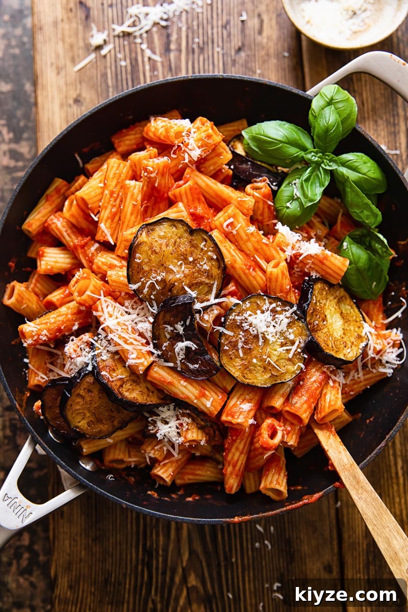 top down view of rigatoni with tomato sauce, topped with sliced of fried eggplant and grated Parmesan