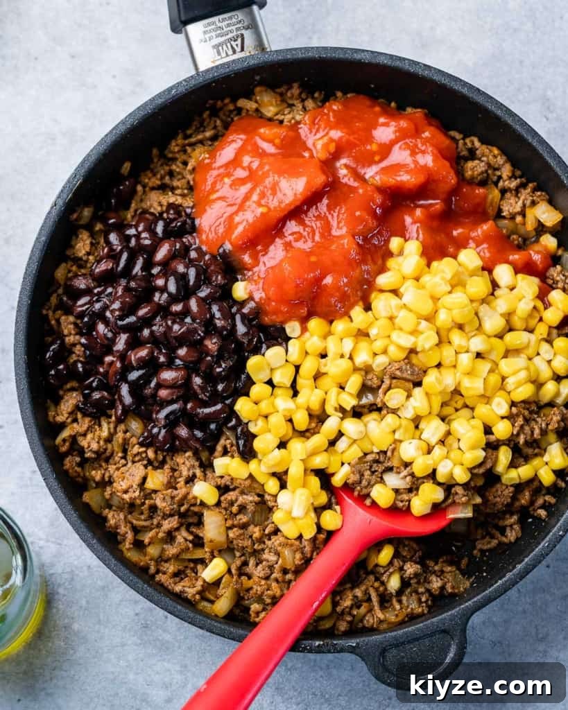 Cheesy Taco Casserole: One-Pan Mexican Dinner Recipe 5 Cooking beef, corn, black beans and tomatoes in a skillet.