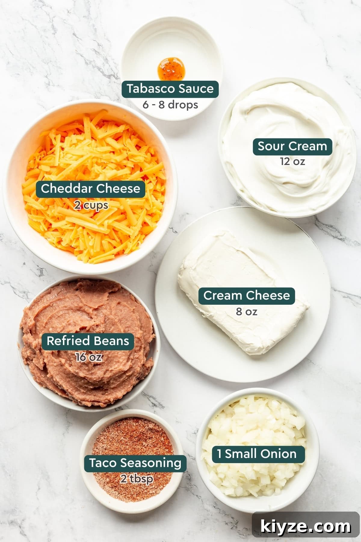 Creamy Cheesy Refried Bean Dip for Parties and Game Day 4 Ingredients for cheesy refried bean dip, including tabasco, sour cream, cheddar, cream cheese, refried beans, taco seasoning, onions.