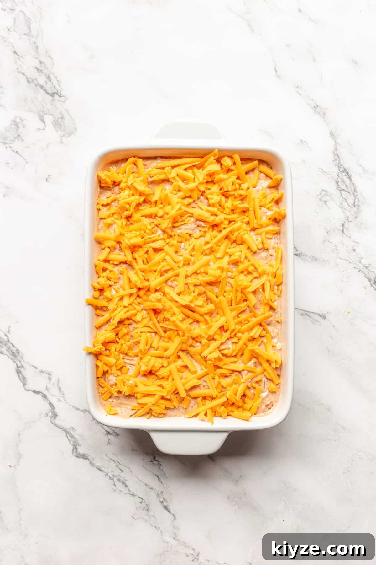 Creamy Cheesy Refried Bean Dip for Parties and Game Day 7 Shredded cheese added to bean dip in dish.
