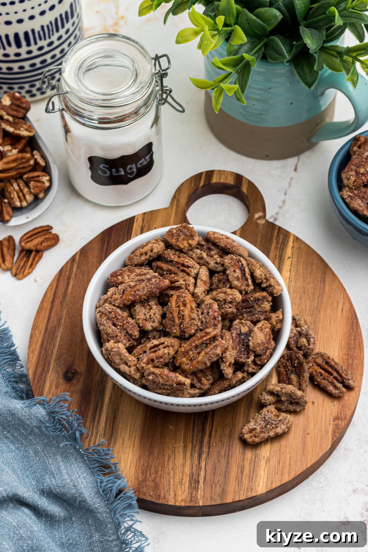 Cinnamon Sugar Candied Pecans Recipe for Snacking & Gifts 2 Sugar coated pecans in a white bowl with a small jar of sugar behind the bowl.