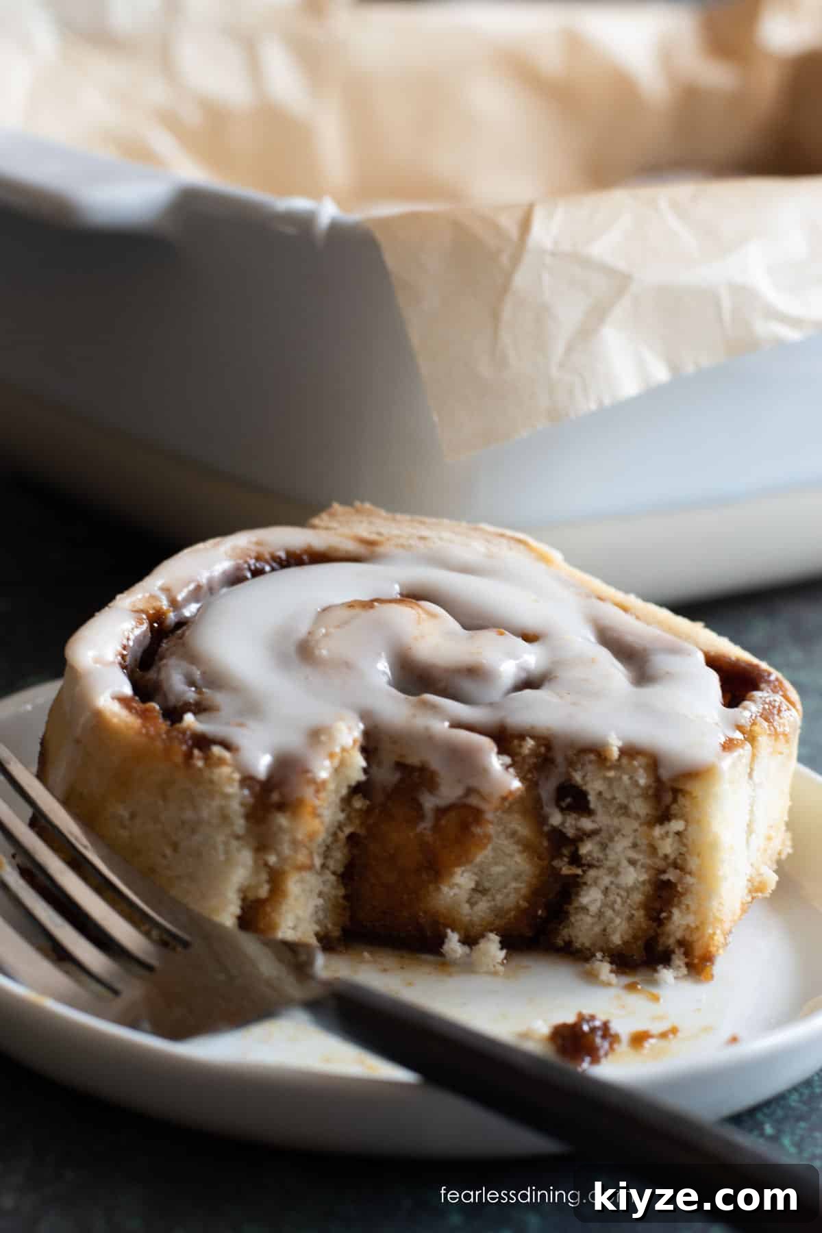 Gluten-Free Gingerbread Cinnamon Rolls Recipe 3 A gluten free gingerbread cinnamon roll on a small white plate. A bite is taken out.