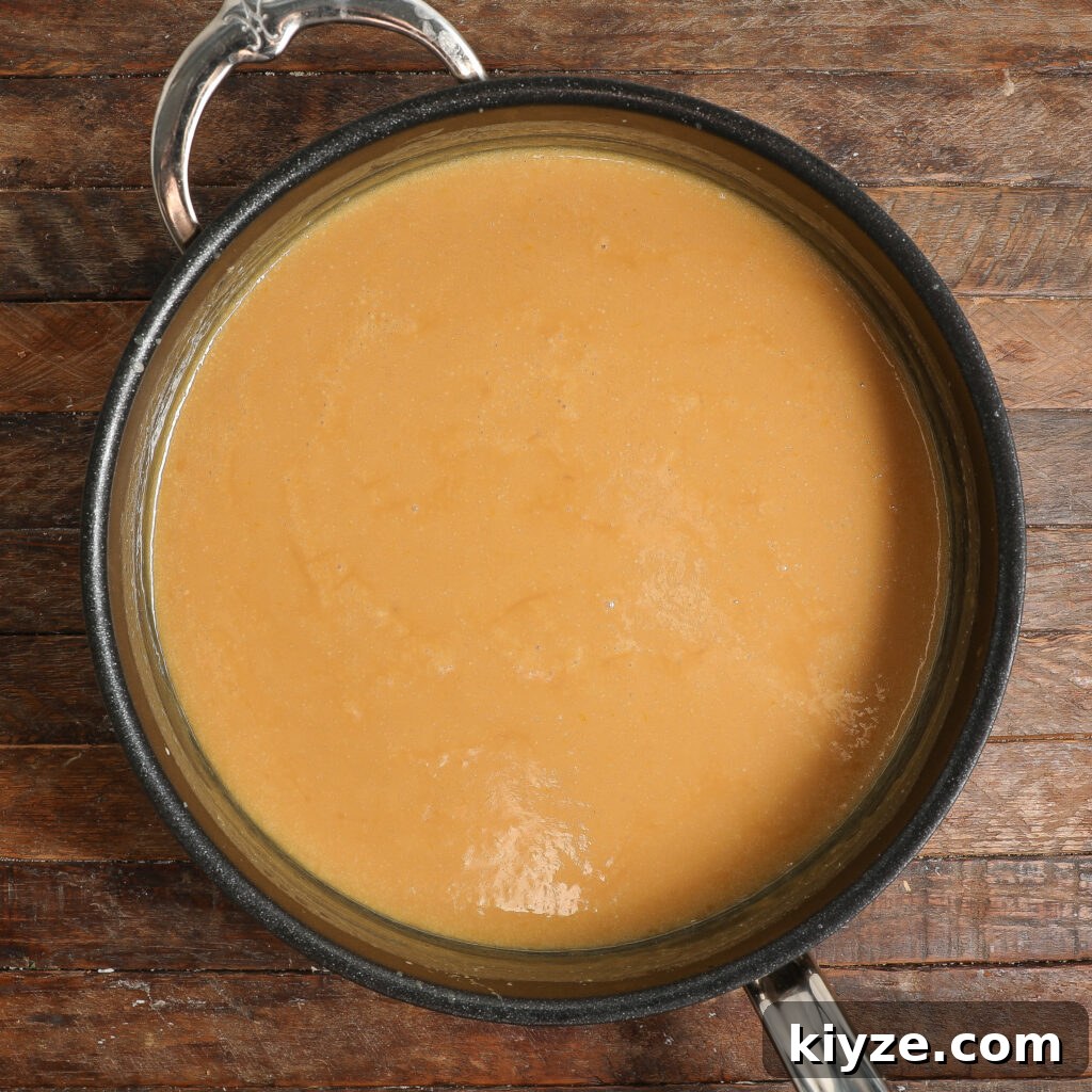 German Chocolate Cake Frosting Recipe: Rich Coconut-Pecan Icing 4 A pot filled with smooth, light brown gravy, reminiscent of German Chocolate Cake Frosting, sits on a rustic wooden surface.