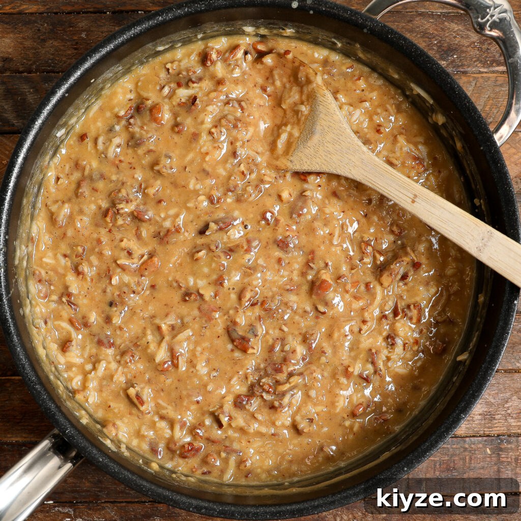 German Chocolate Cake Frosting Recipe: Rich Coconut-Pecan Icing 6 A pot filled with rich German Chocolate Cake Frosting, showing a thick, creamy mixture with chopped pecans and shredded coconut, stirred with a wooden spoon on a dark wooden surface.
