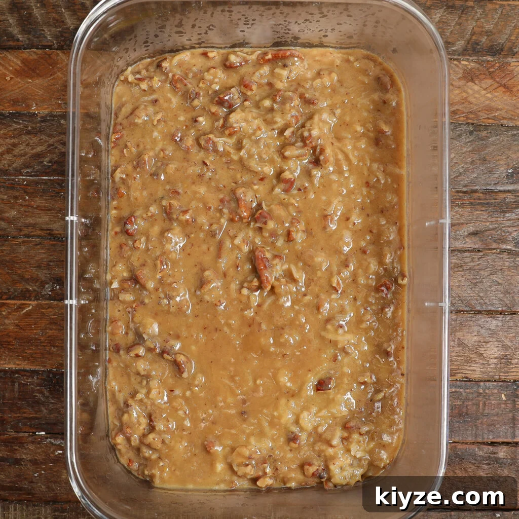 German Chocolate Cake Frosting Recipe: Rich Coconut-Pecan Icing 7 A rectangular glass dish filled with a thick, light brown German Chocolate Cake Frosting, studded with visible chunks of pecans, sits on a rustic wooden surface.