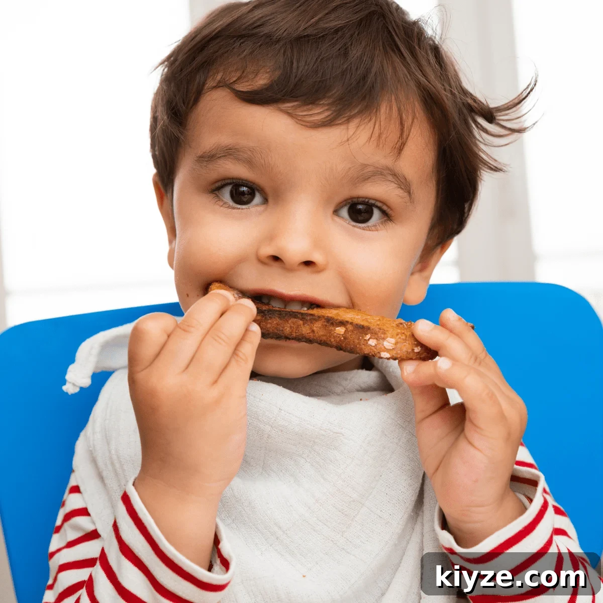 Prevent Toddler Grazing: Simple Strategies to Curb Constant Snacking 6 Sitting child wearing a bib and eating a piece of bread