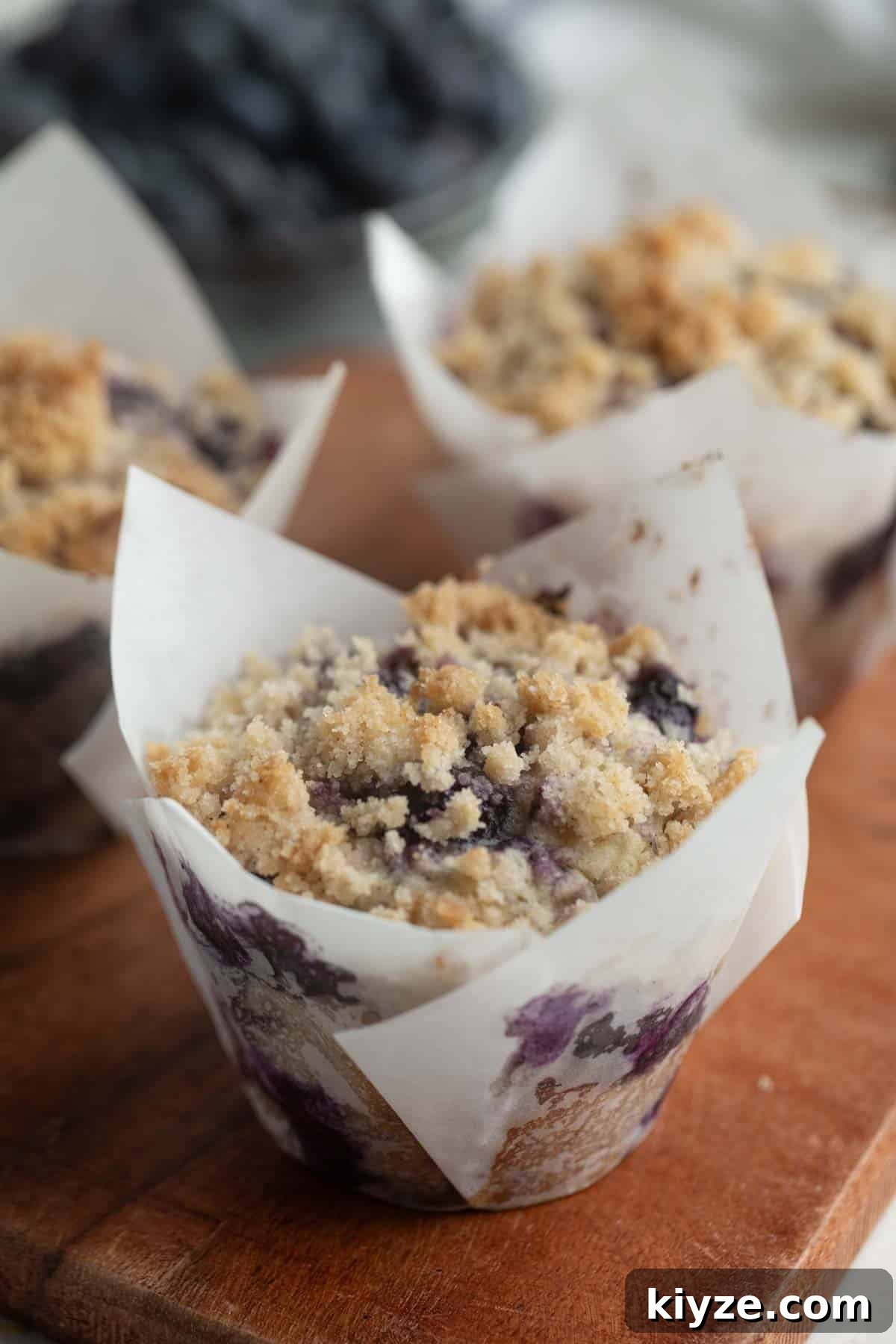 Blueberry Muffin Recipe: Moist, Bursting-with-Fruit Breakfast Muffins 9 Blueberry Muffins with crumb topping on a wooden board.