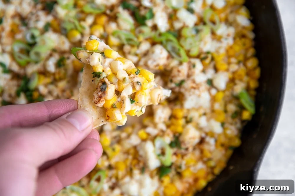 Jalapeño Feta Elote Dip Recipe for Parties and Game Day 2 Hand holding tortilla chip topped with Mexican street corn dip.