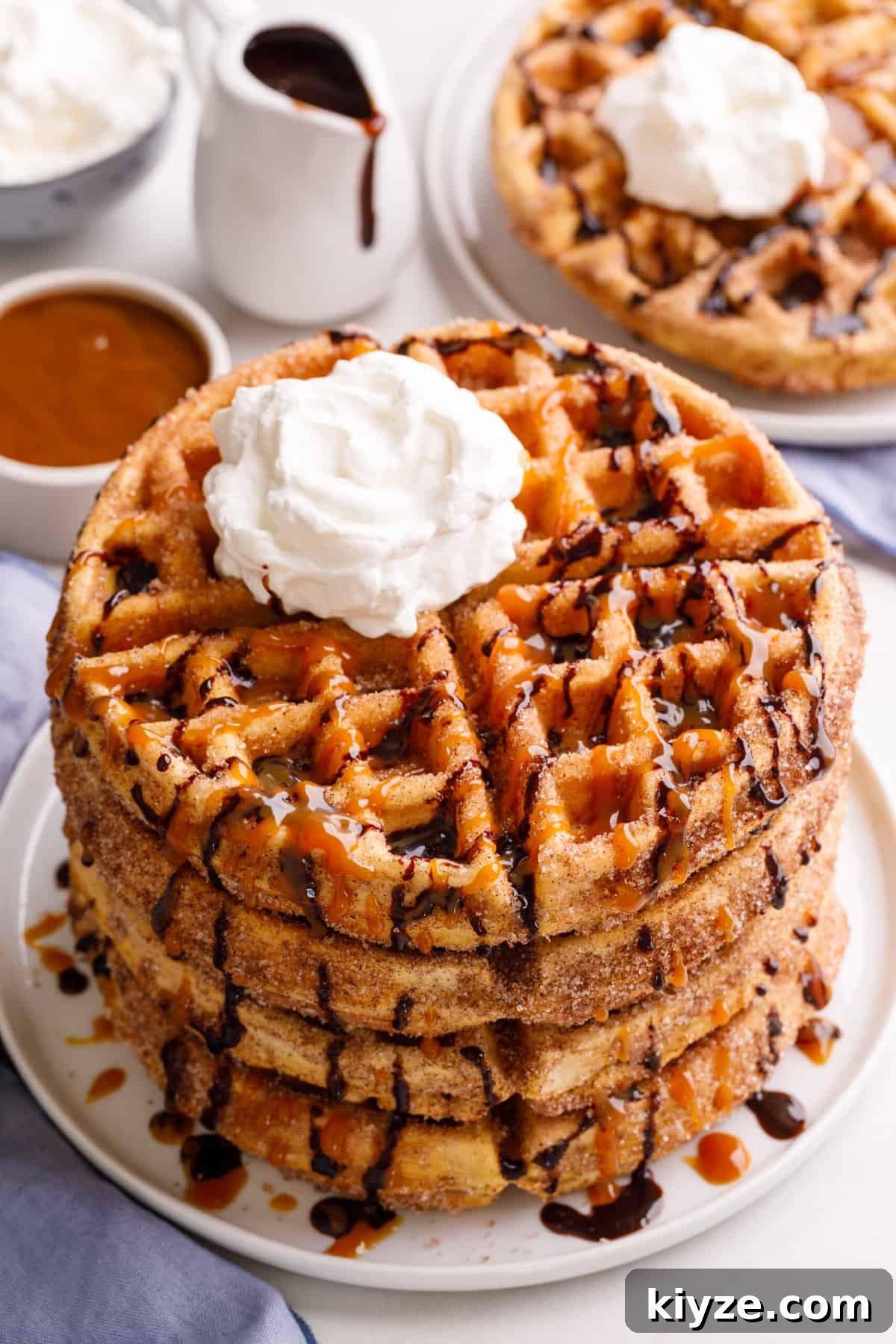Crispy Cinnamon Churro Waffles Recipe 2 stack of four churro waffles on a plate topped with chocolate and caramel sauce and whipped cream.