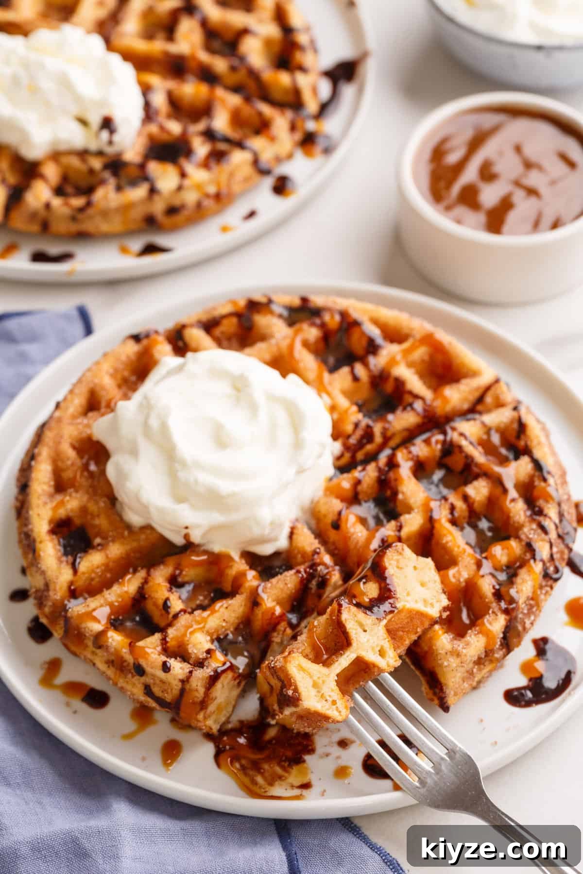 serving of churro waffle on a white round plate topped with chocolate sauce, dulche de leche and whipped cream.