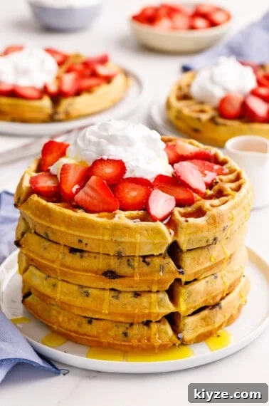 A stack of four chocolate chip waffles topped with strawberries and whipped cream.