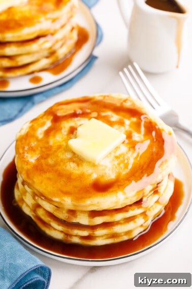 A stack of overnight pancakes on a plate topped with butter and syrup.